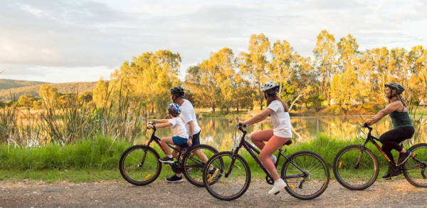 Image of three children riding bikes down a country road with an adult walking next to them